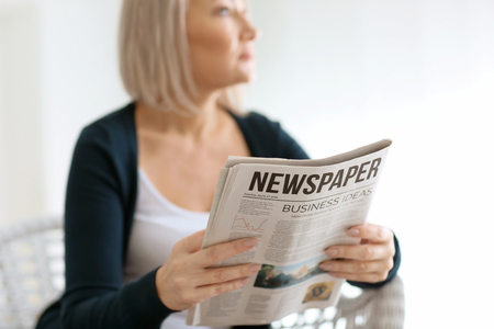 Mature woman with newspaper at home