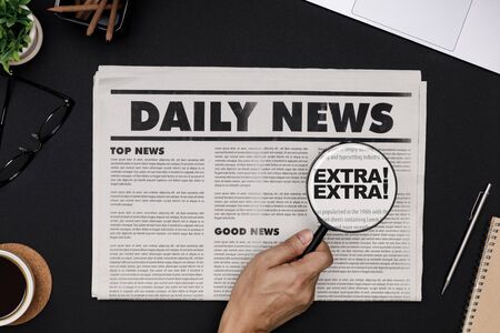 Hand using magnifying glass at business newspaper and office supplies with notebook hot coffee cup glasses books and accessories on black desk topview daily newspaper mockup concept