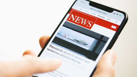 Online news on a smart phone businessman reading news or article on a mobile phone screen app hand holding smart device newspaper and portal on internet displayed news are not reality related Stock Photo
