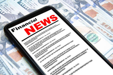The smartphone on the screen the inscription financial news lies on dollars 100 dollars banknotes and smartphone with financial news Stock Photo