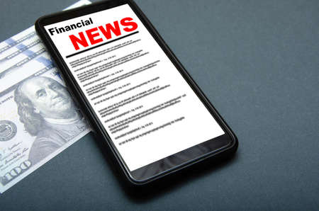 The smartphone on the screen the inscription financial news lies on dollars 100 dollars banknotes and smartphone with financial news Stock Photo