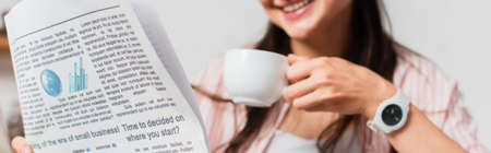 Panoramic crop of brunette woman holding cup and newspaper