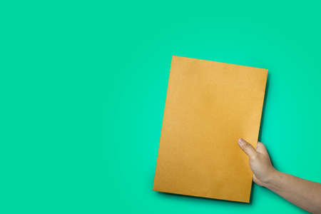 Close up of hand holding a brown envelope a4 size paper envelope isolated on green background