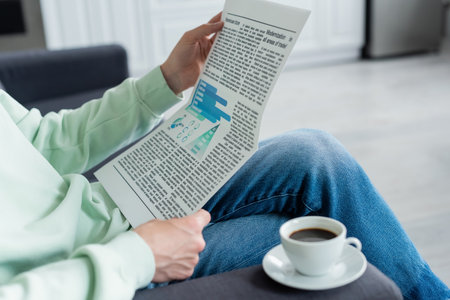 Cropped view of man reading newspaper near coffee cup on sofa