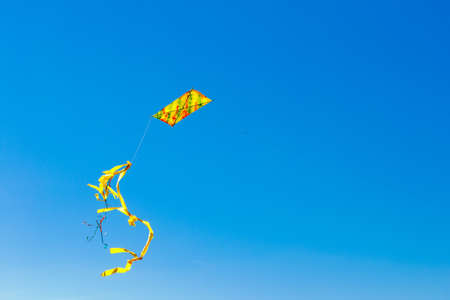 colorful yellow kite with tail in blue sky
