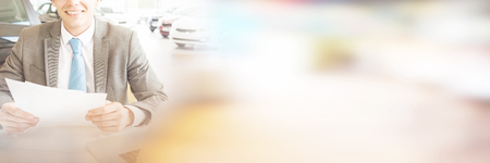 Portrait of smiling salesman reading document while sitting at car showroom Stock Photo