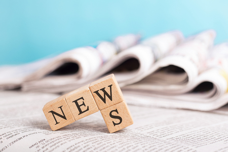 News word writing on cube front newspaper stack